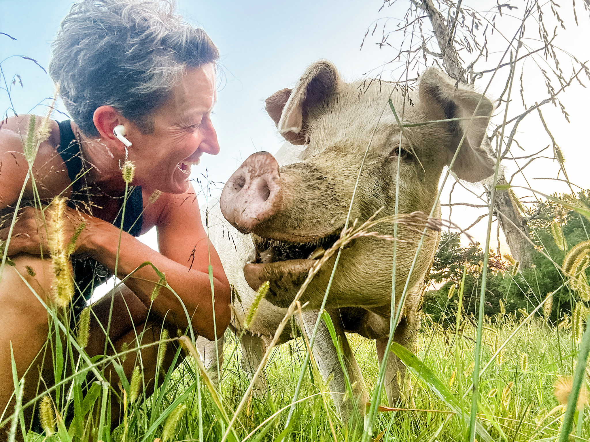 Dudley standing in tall grass beside a smiling caregiver, with mud on his face.